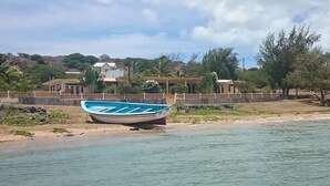A boat on a calm body of water with a house and trees in the background.