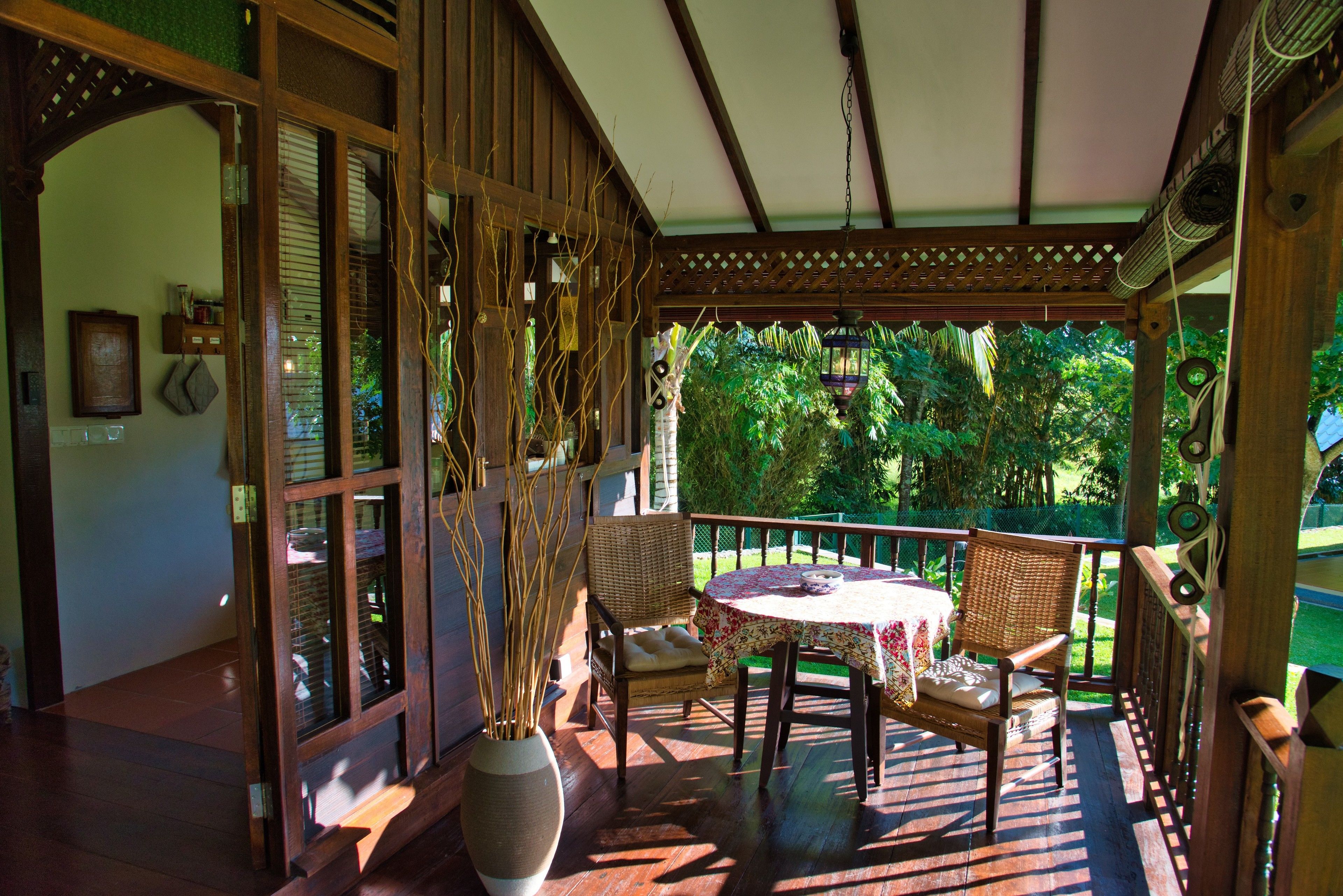 A wooden porch with a table and chairs, a large vase with branches, and a view of greenery.