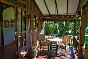 A wooden porch with a table and chairs, a large vase with branches, and a view of greenery.
