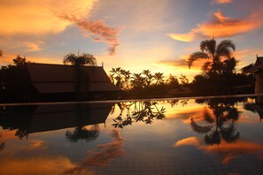 A serene pool area with reflections of palm trees and a traditional building at sunset.