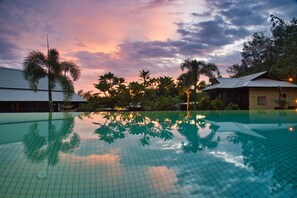 An infinity pool reflecting palm trees and a sunset sky.