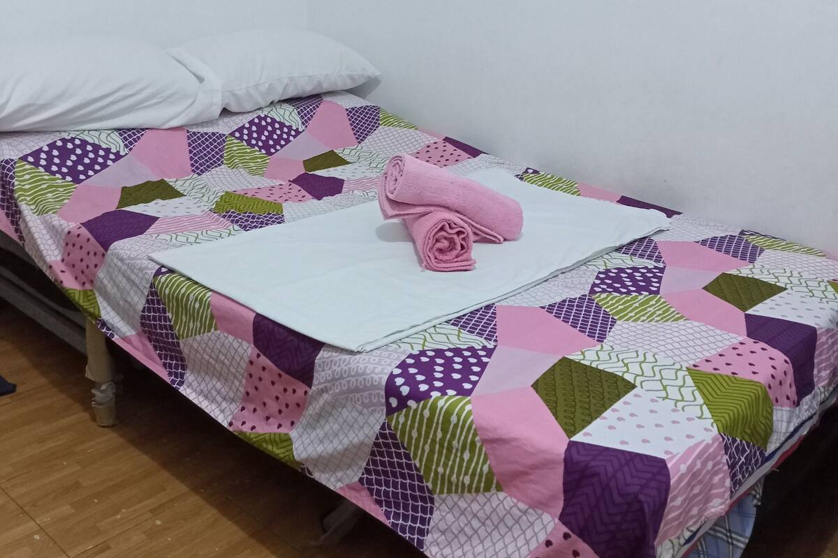 Una cama individual con un edredón colorido y una toalla rosa enrollada.