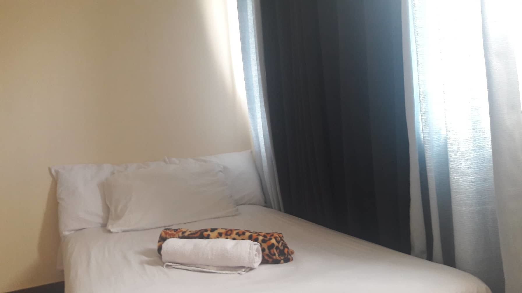 A bed with white linens, a leopard print pillow, and a folded towel.