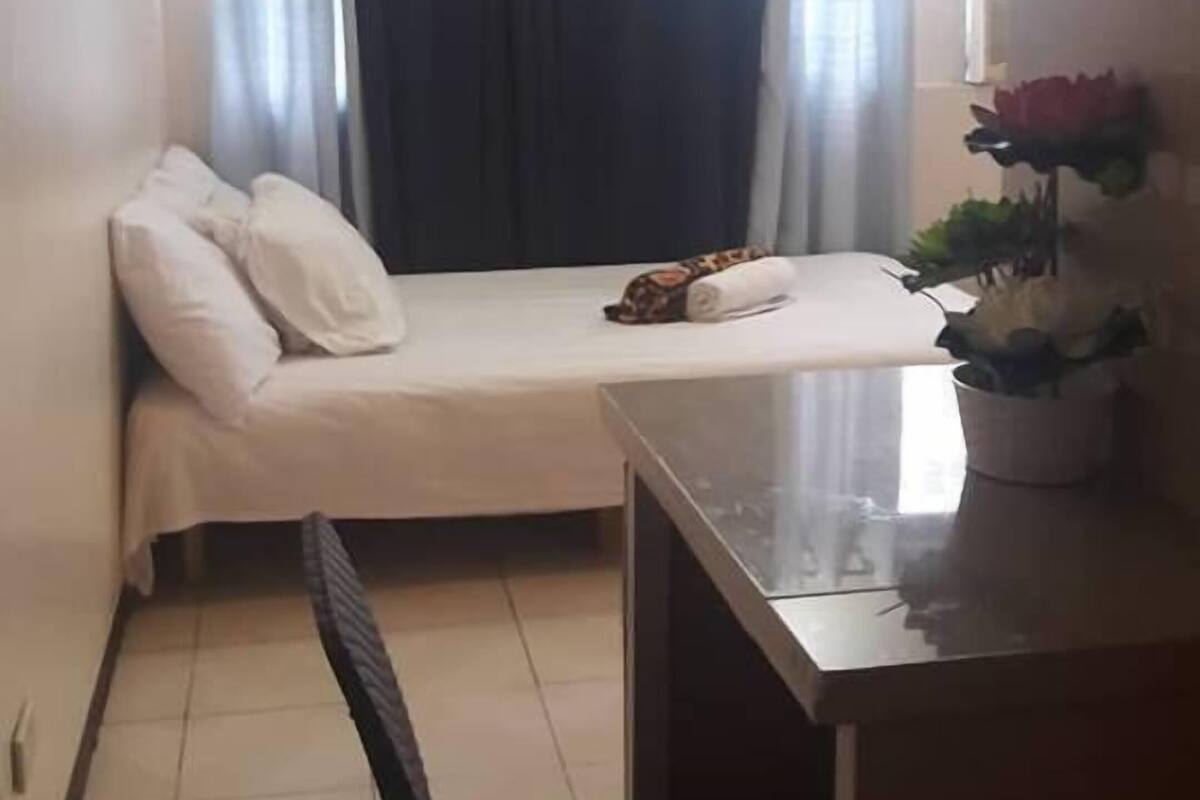 Una habitación pequeña con cama, escritorio, silla y ventana con cortinas.