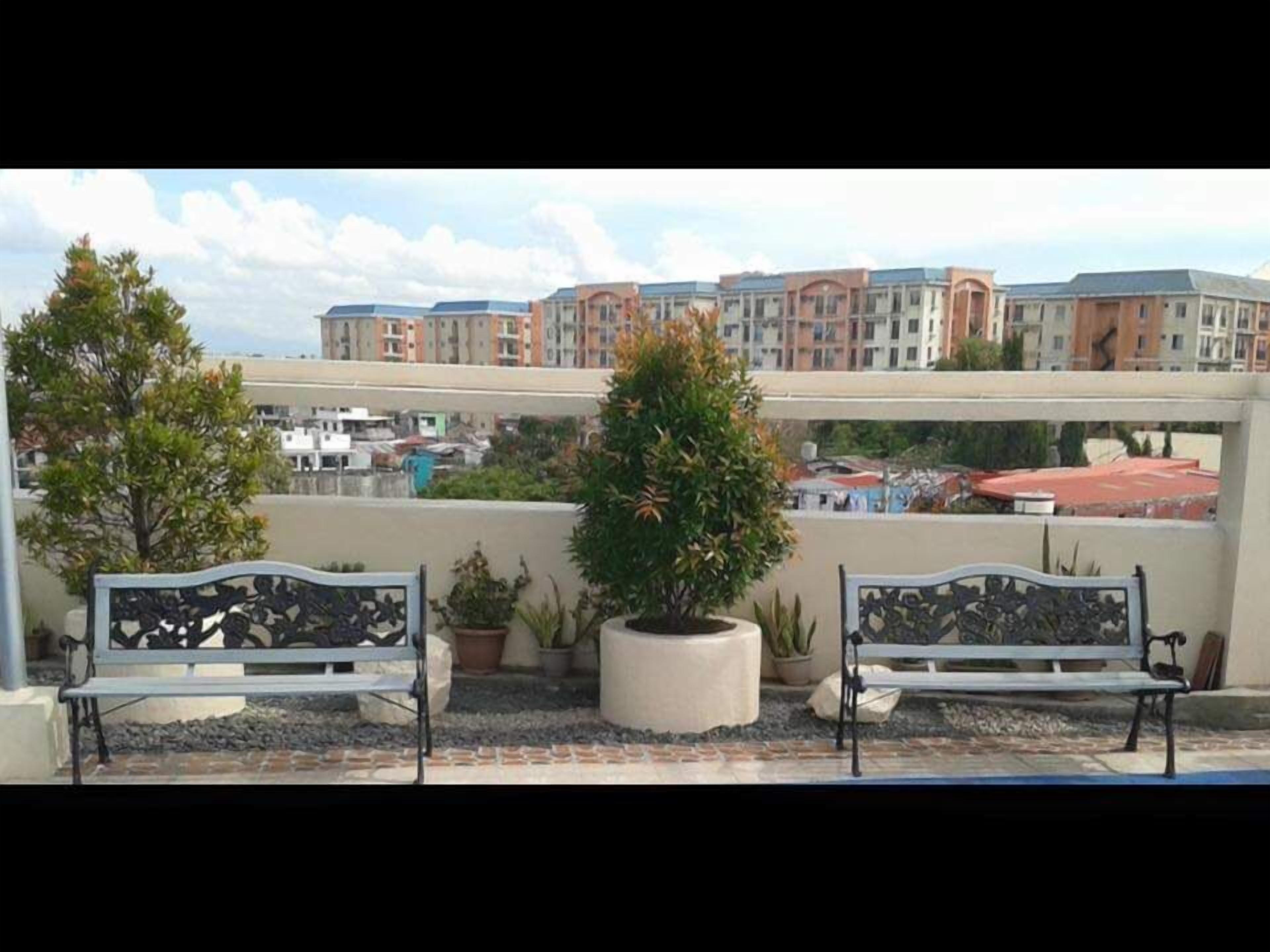 A rooftop terrace with two benches, potted plants, and a view of residential buildings.