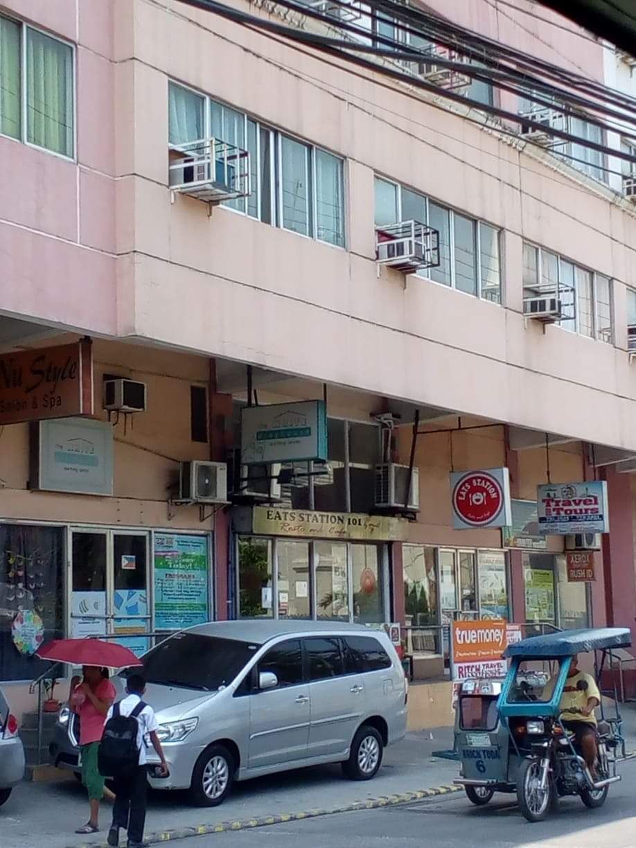 A building with multiple signs, including a radio station and a travel agency. There is a parked car and a motorcycle in front.