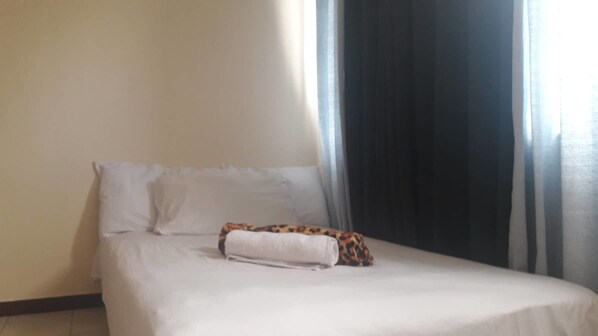 Una cama con sábanas blancas y un cojín estampado de leopardo.