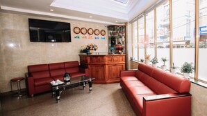 Eine Lobby mit roten Sofas, einem Couchtisch, einem an der Wand befestigten Fernseher und einer Holztresen mit Blumentöpfen.
