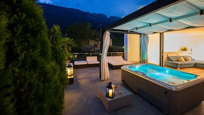 Un espace extérieur aménagé avec un jacuzzi, des sièges et une piscine, le tout entouré d’arbres et dominé par un paysage montagneux.