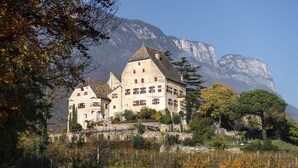 Un grand bâtiment à étages, doté d’un toit en pente, entouré d’arbres et de montagnes.