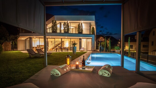 Une maison moderne dotée d’une piscine, d’un espace extérieur aménagé et d’un patio bien éclairé.