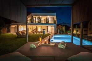 Une maison moderne dotée d’une piscine, d’un espace extérieur aménagé et d’un patio bien éclairé.