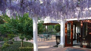 Un espacio de estar al aire libre cubierto con columnas blancas, sillas verdes y una mesa.