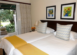 Un lit double avec une literie blanche et jaune, une table de chevet avec une lampe, et deux tableaux encadrés représentant des tournesols accrochés au mur.