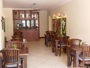A dining area with wooden tables and chairs, a bar with glass cabinets, and a ceiling fan. - 174 Premier Guesthouse (Pretoria)