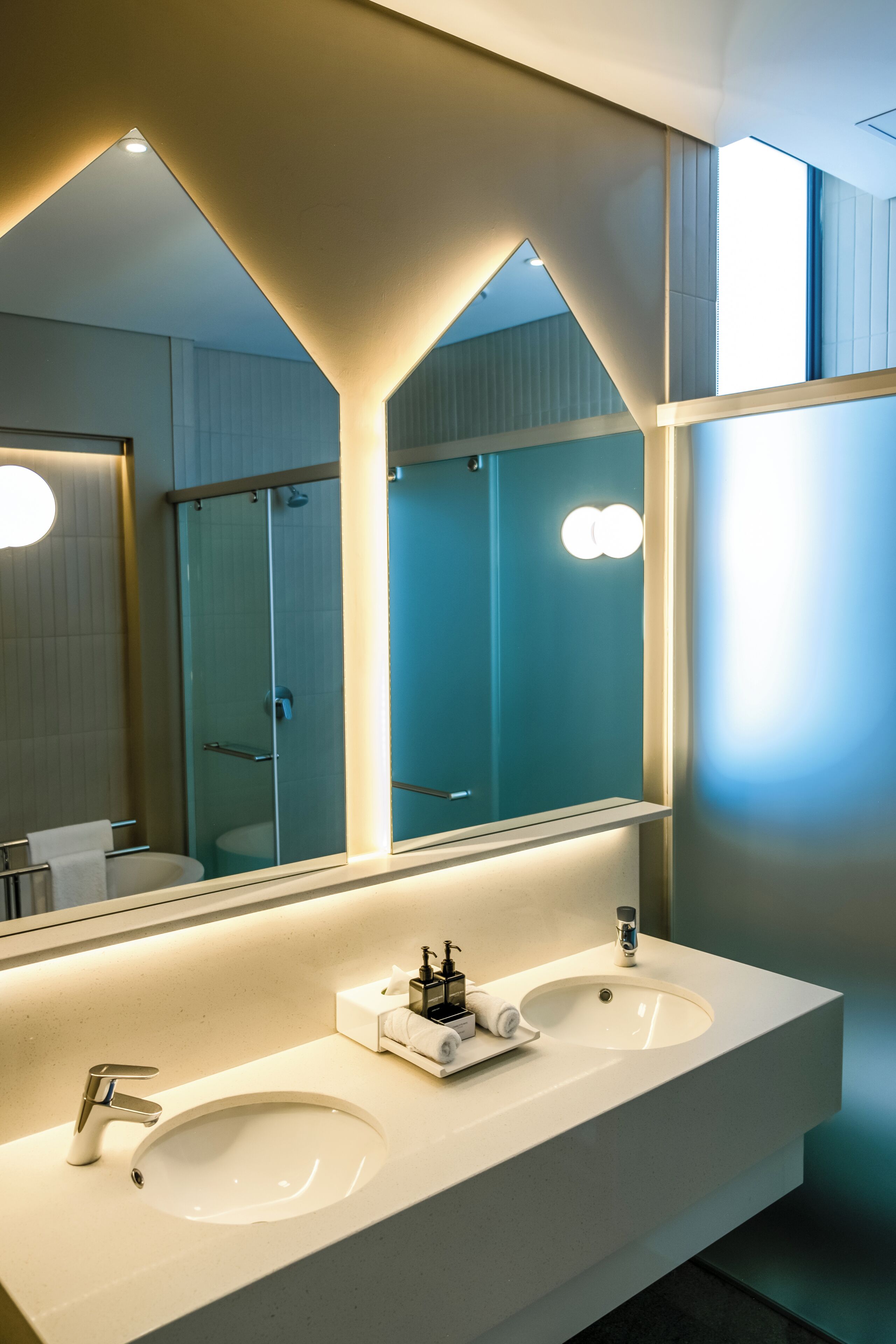 Un baño moderno con dos lavamanos, un espejo grande y una cabina de ducha con mampara de cristal.