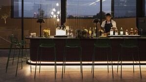 A modern bar with a bartender, bar stools, and a variety of bottles and glasses.