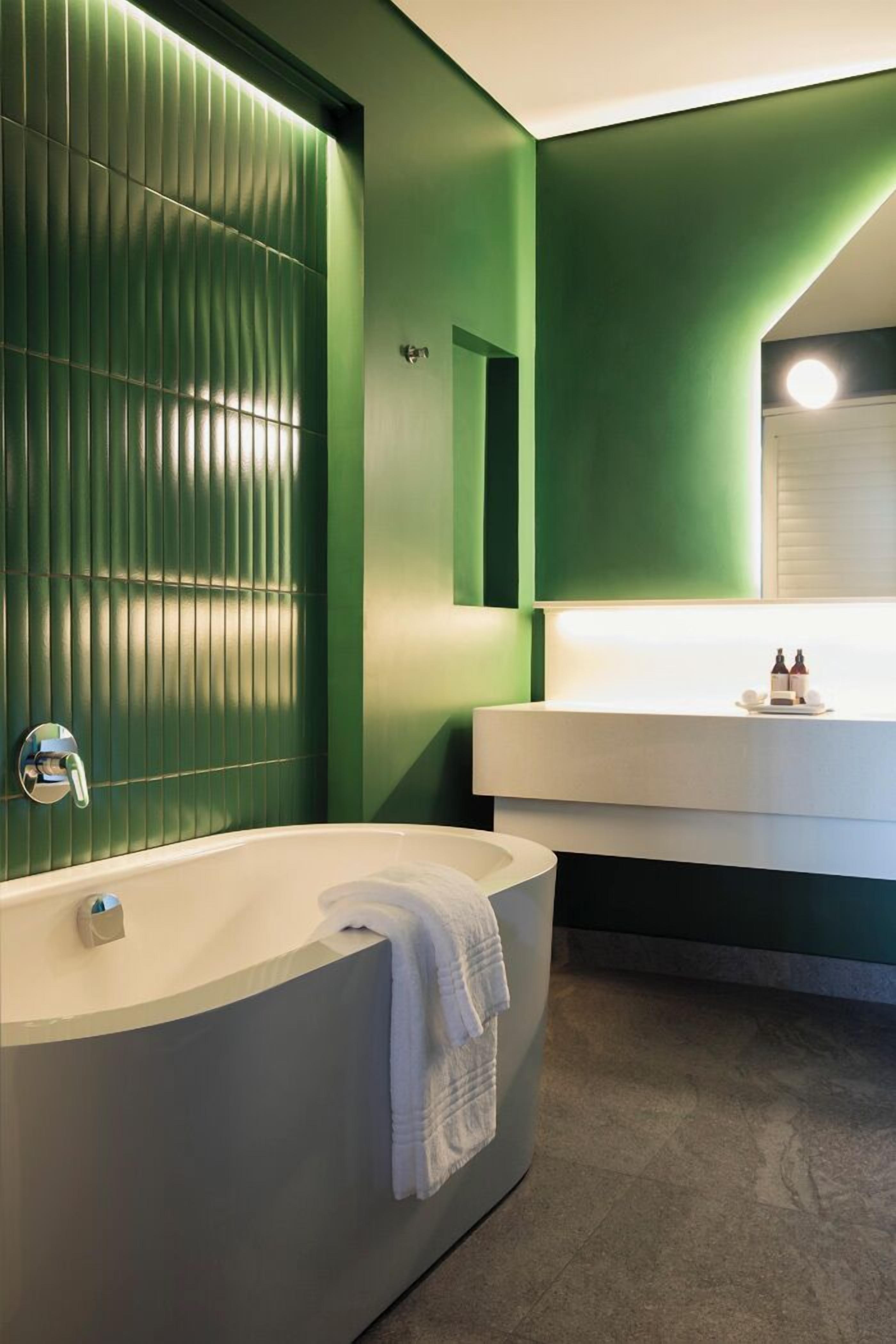 Een moderne badkamer met een ruime badkuip, een wit wastafelmeubel en groene wanden.