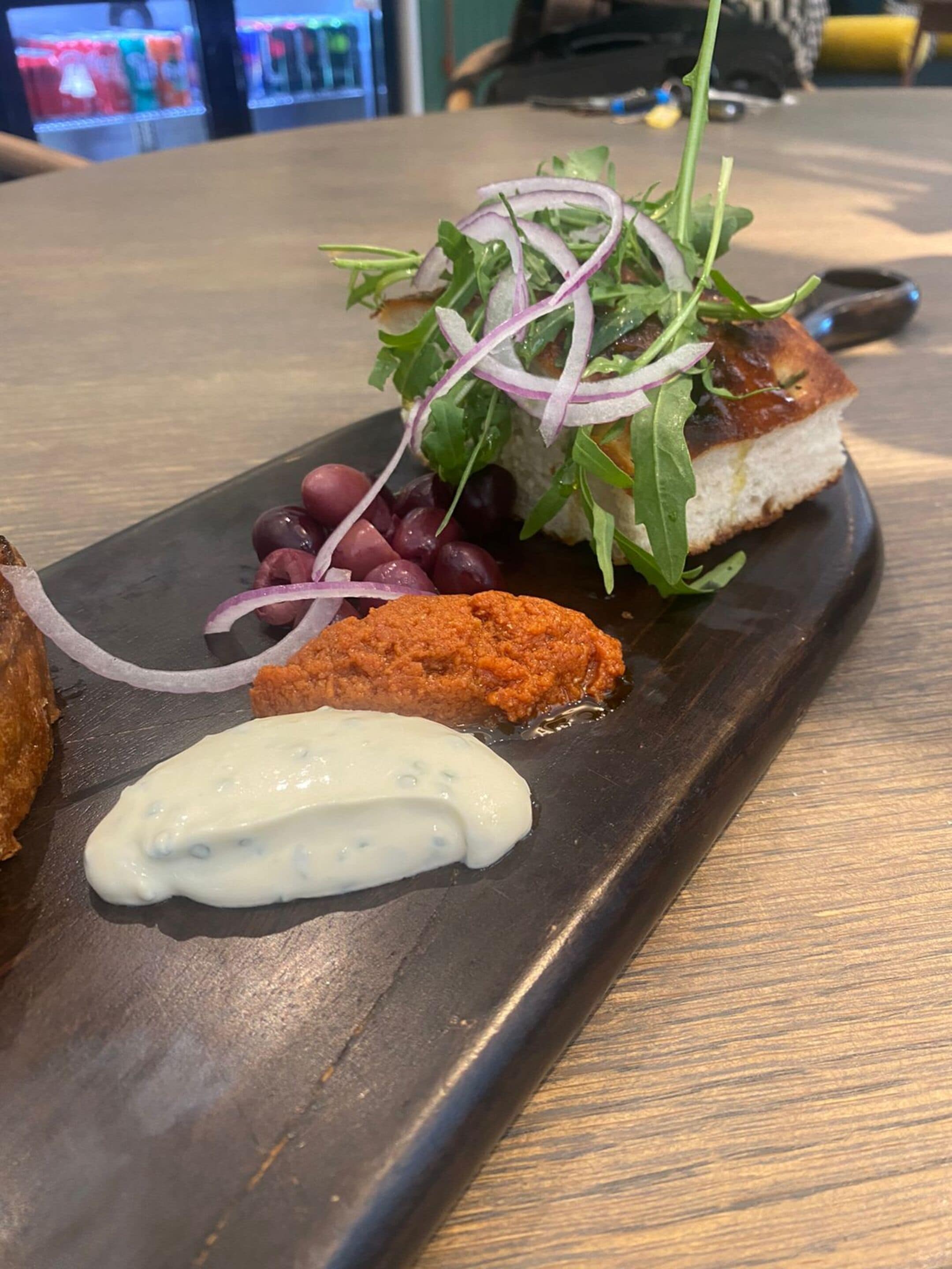 A meal with bread, greens, red onions, grapes, and a creamy sauce on a slate serving board.