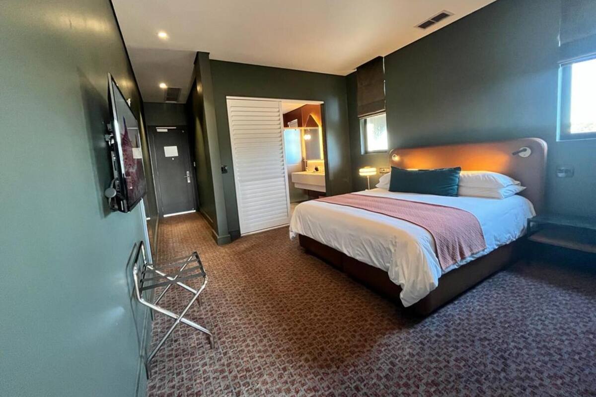 Une chambre d’hôtel avec un grand lit, un téléviseur fixé au mur, un miroir et un petit coin salon.