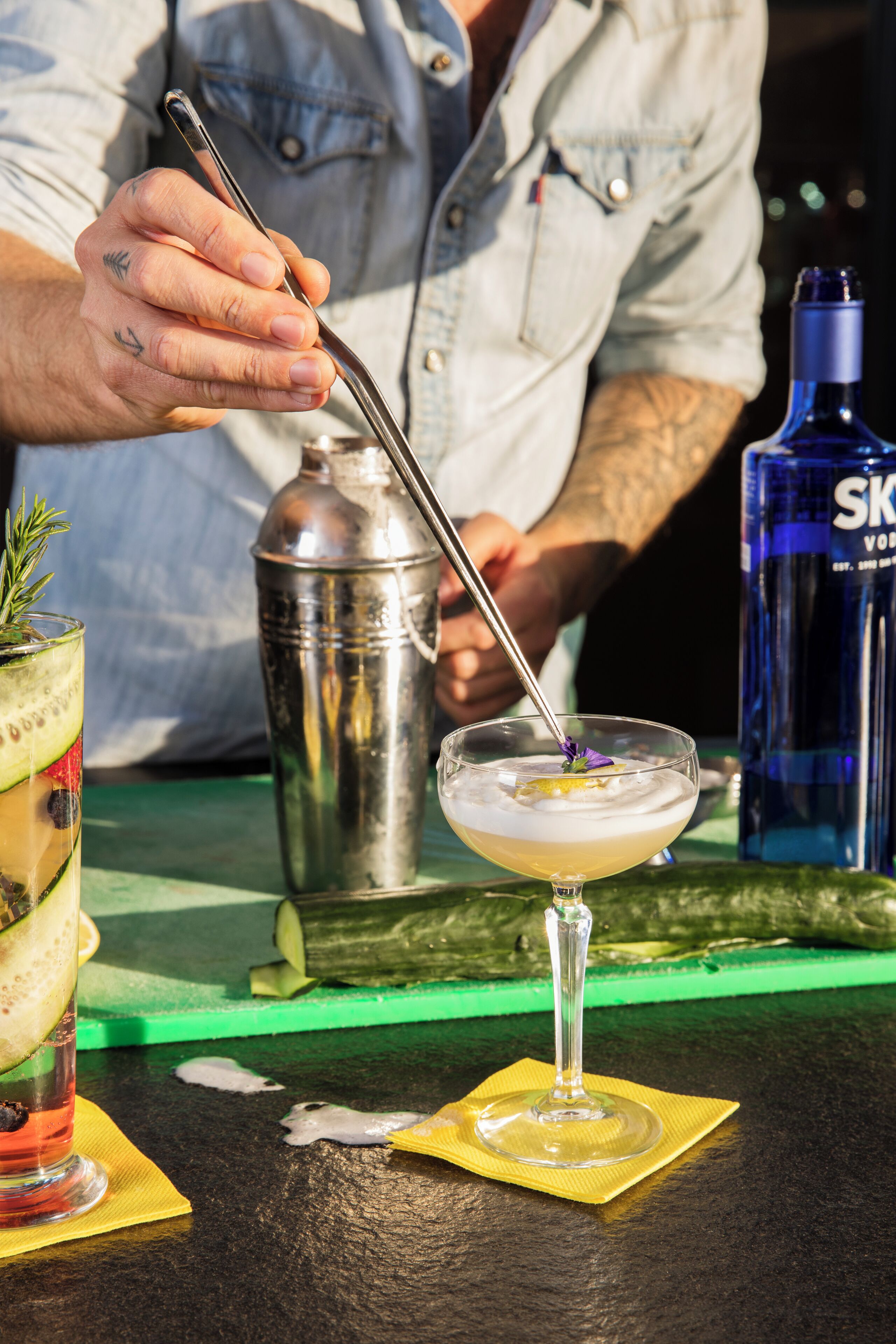 A bartender preparing a cocktail with a shaker and a bottle of vodka in the background.