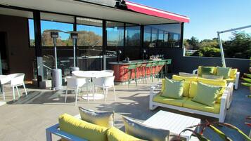 Terraza en la azotea con mobiliario exterior, zona de bar y cerramiento de cristal.