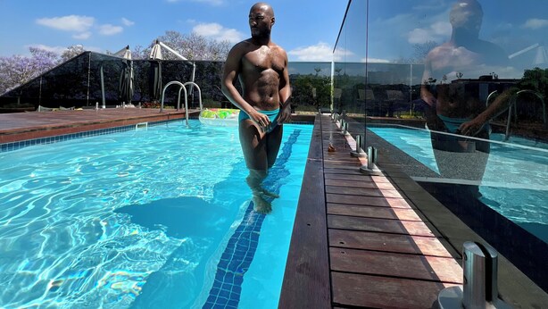 A swimming pool with clear blue water, a wooden deck, and a glass railing.