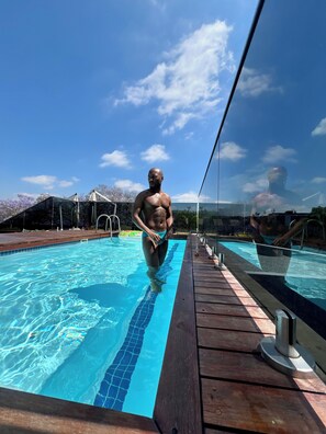 Una piscina con agua azul cristalina, un muelle de madera y barandilla de vidrio.