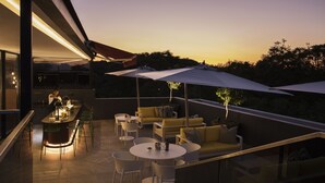 A modern outdoor dining area with a bar, yellow sofas, and umbrellas.