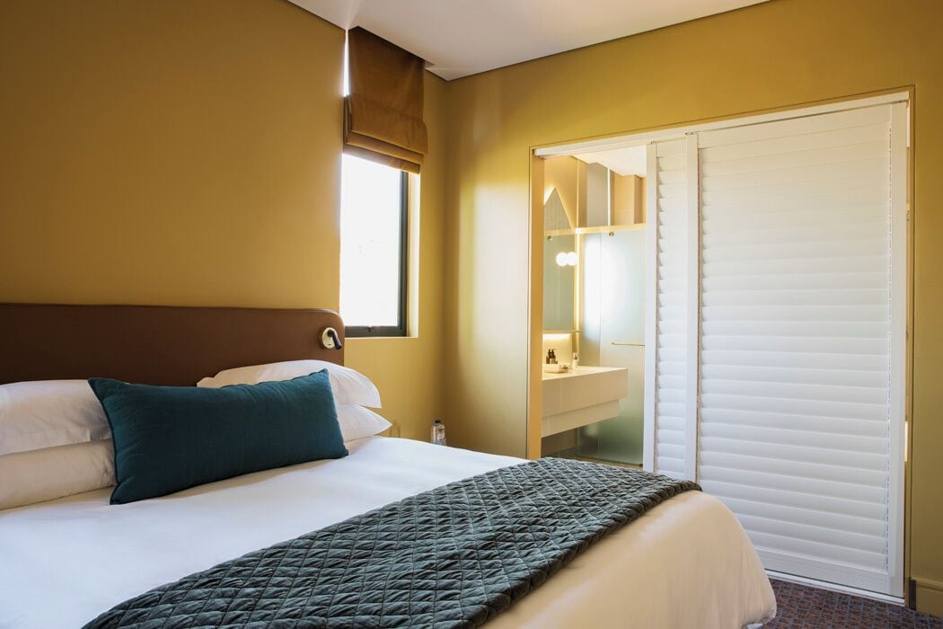 Una habitación de hotel con cama, ventana con vistas, baño con espejo y puerta corredera.