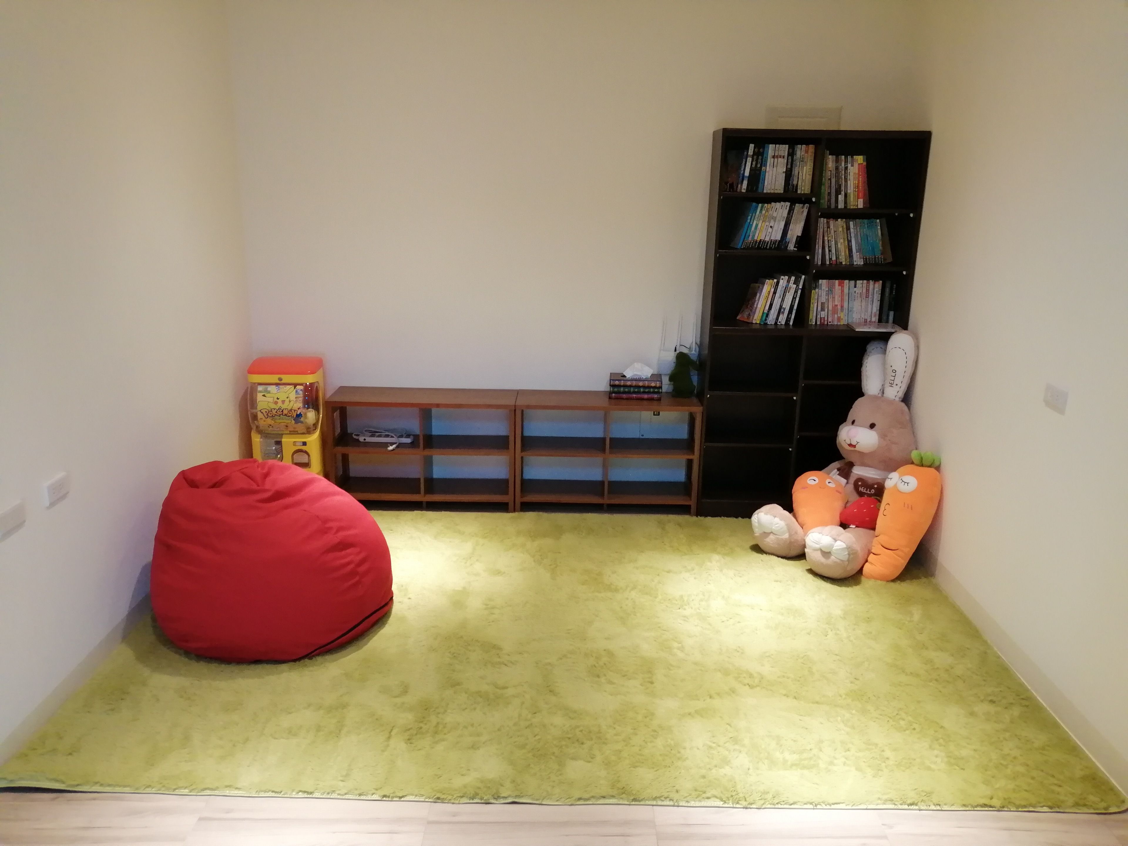 Una habitación con alfombra verde, un sillón informal de tela roja, una estantería y un conejo de peluche.