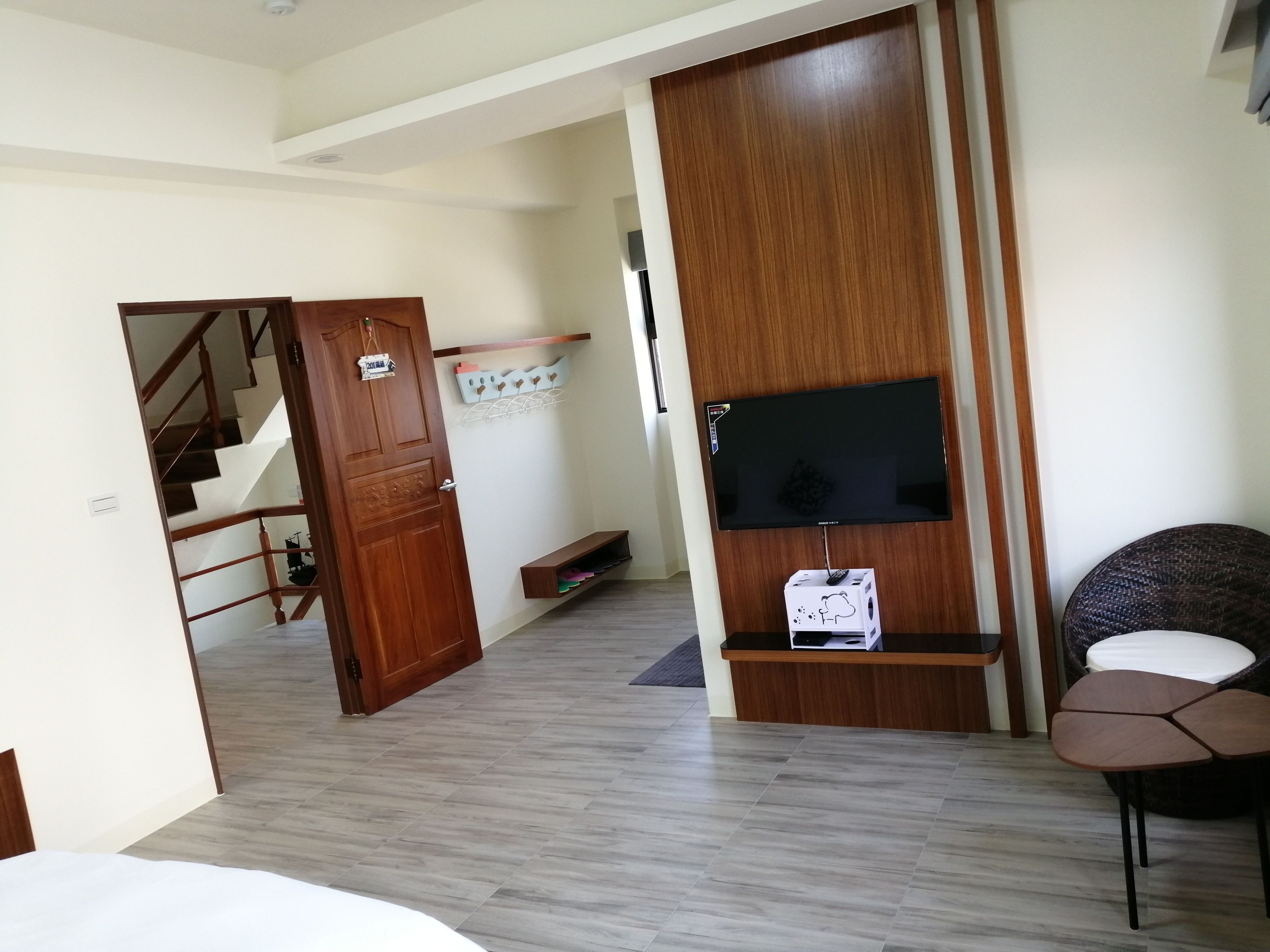 A hotel room with a wooden wardrobe, a TV mounted on the wall, a small shelf, a chair, and a staircase leading to another room.