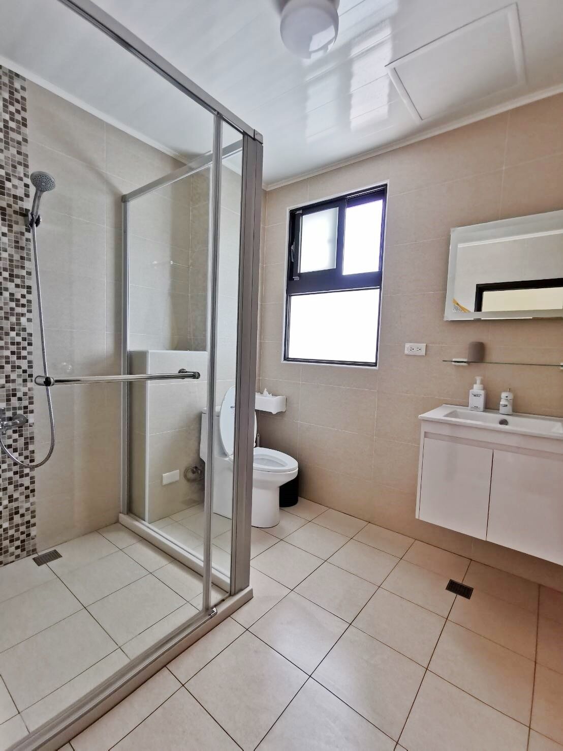 Un baño moderno con cabina de ducha de vidrio, inodoro, lavamanos y ventana.