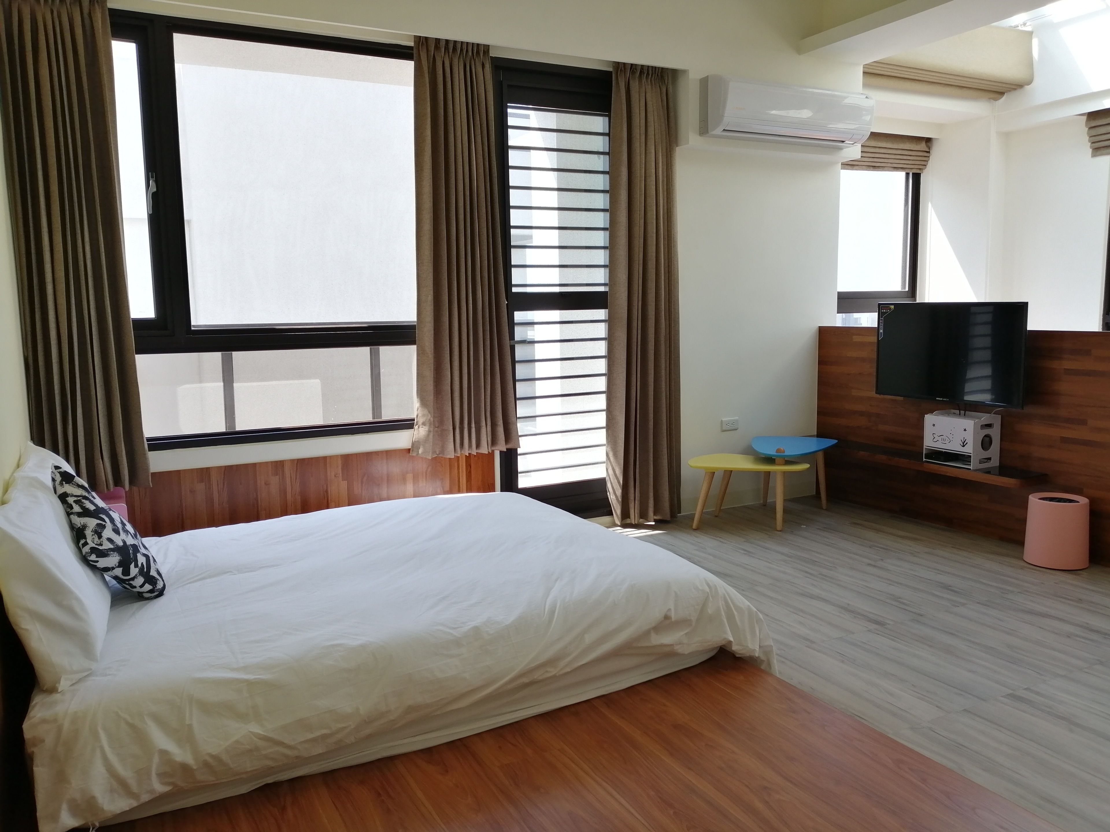 A hotel room with a bed, a television, a small table, and an air conditioning unit.