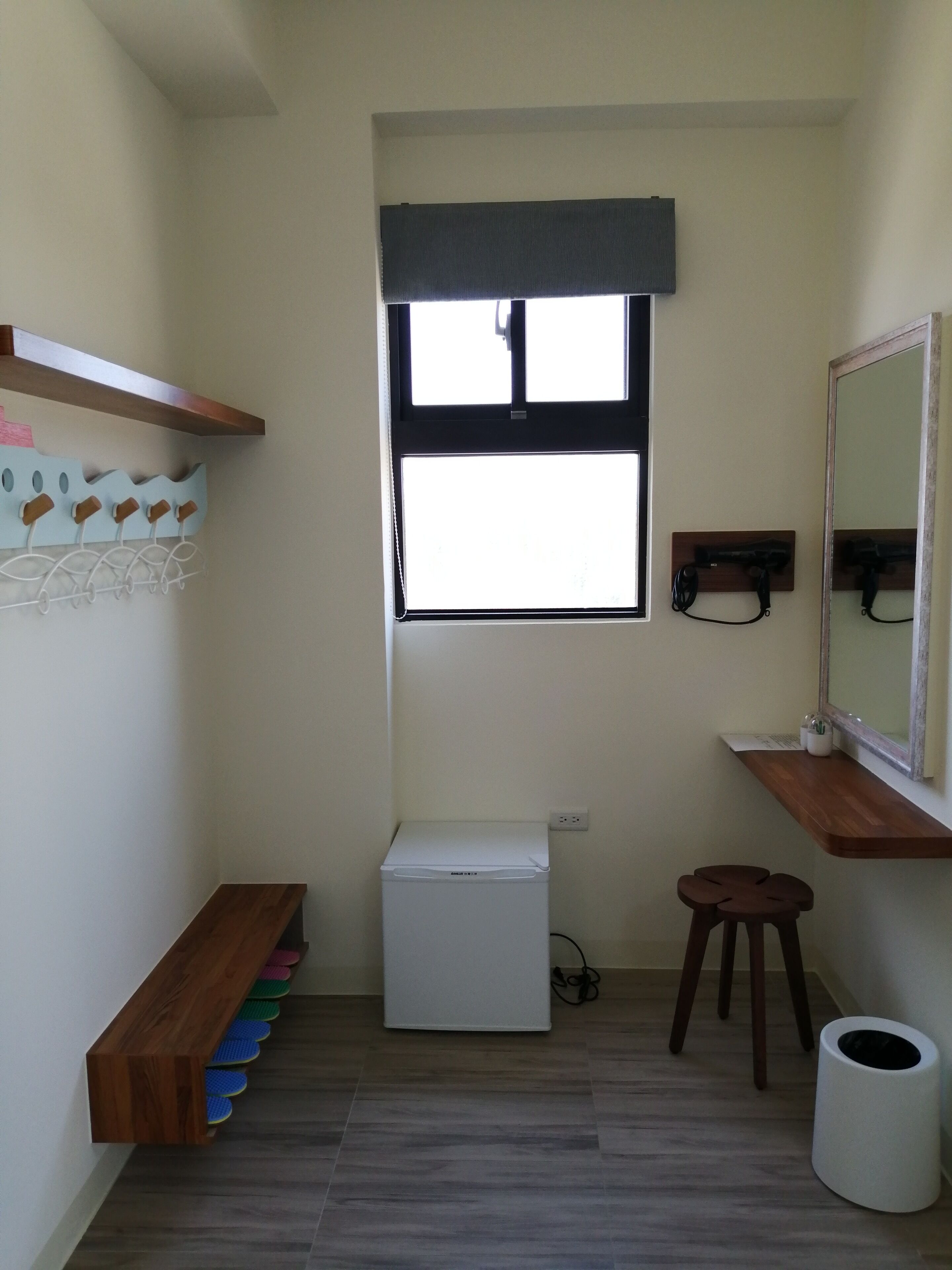 A compact room with a built-in washing machine, a small stool, a mirror, and a shelf with hooks.