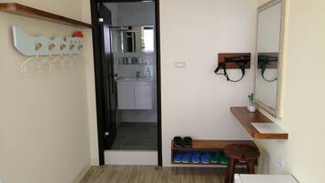 A compact bathroom with a shower, a sink, and a mirror. There is a shelf with shoes and a small table with a hairdryer.