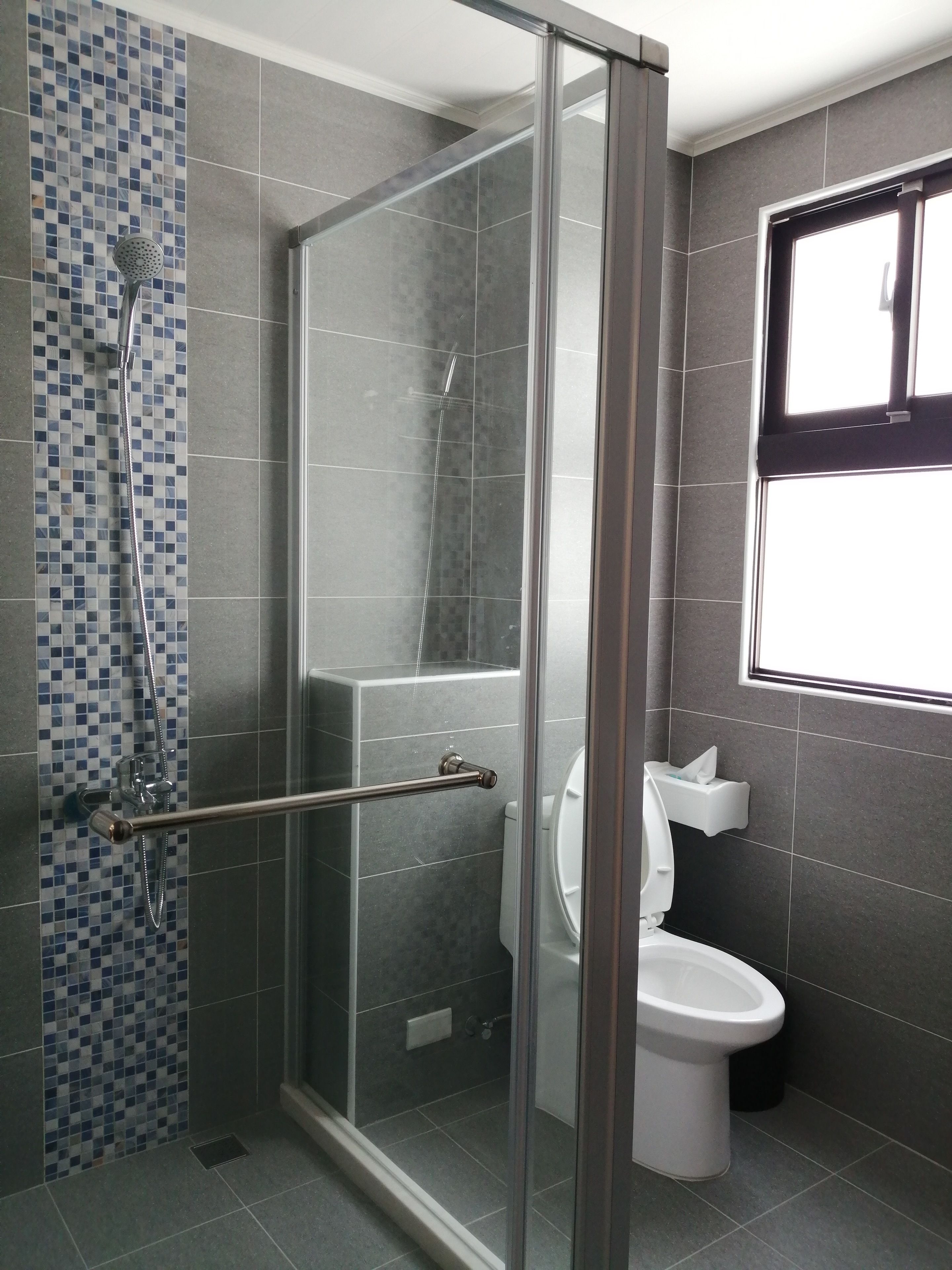 A modern bathroom with a glass shower enclosure, a toilet, and a window.