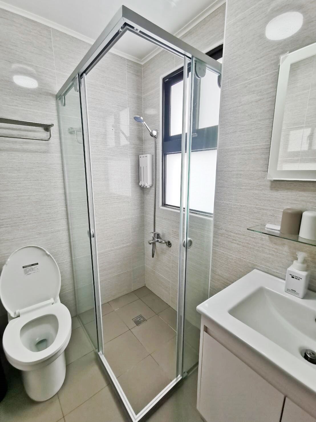 A modern bathroom with a glass-enclosed shower, a white toilet, and a sink with a mirror above it.