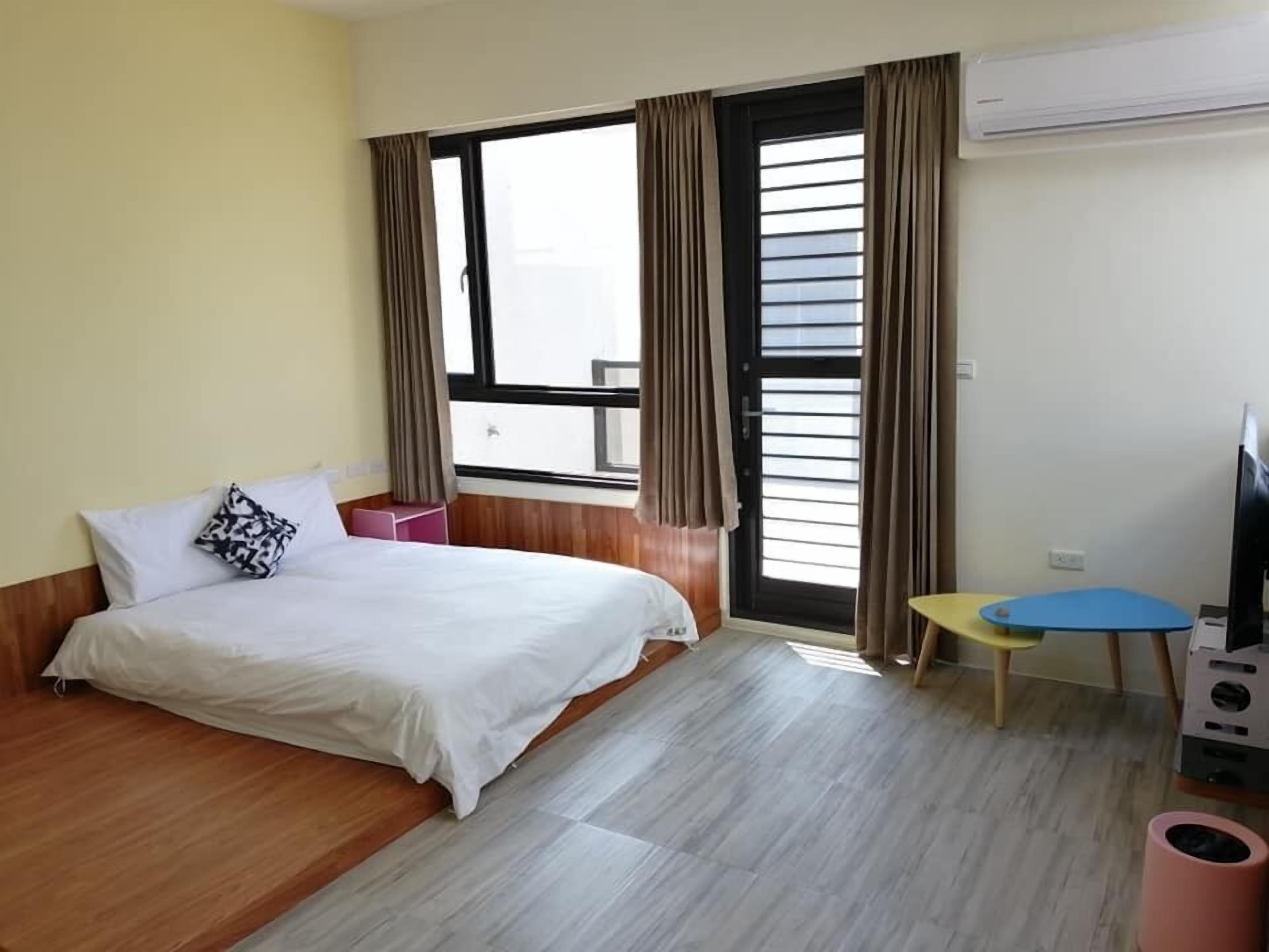Habitación de hotel con cama, una mesita, una silla, equipo de aire acondicionado y ventana con cortinas.