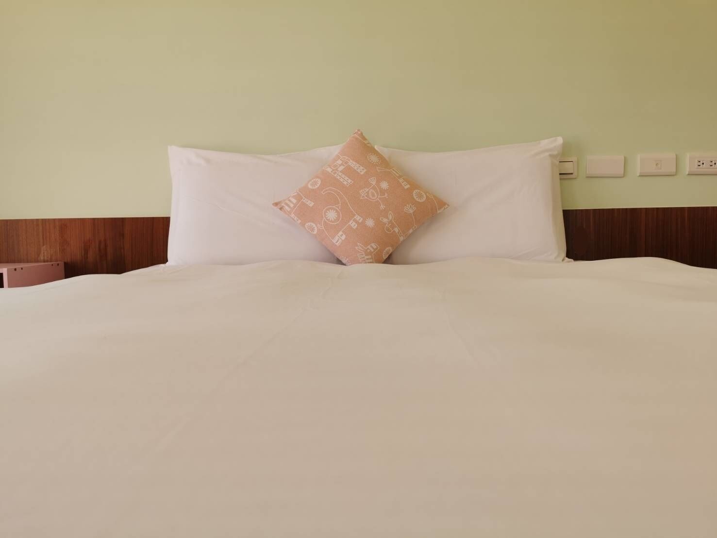 A neatly made bed with white linens and a single patterned pillow.