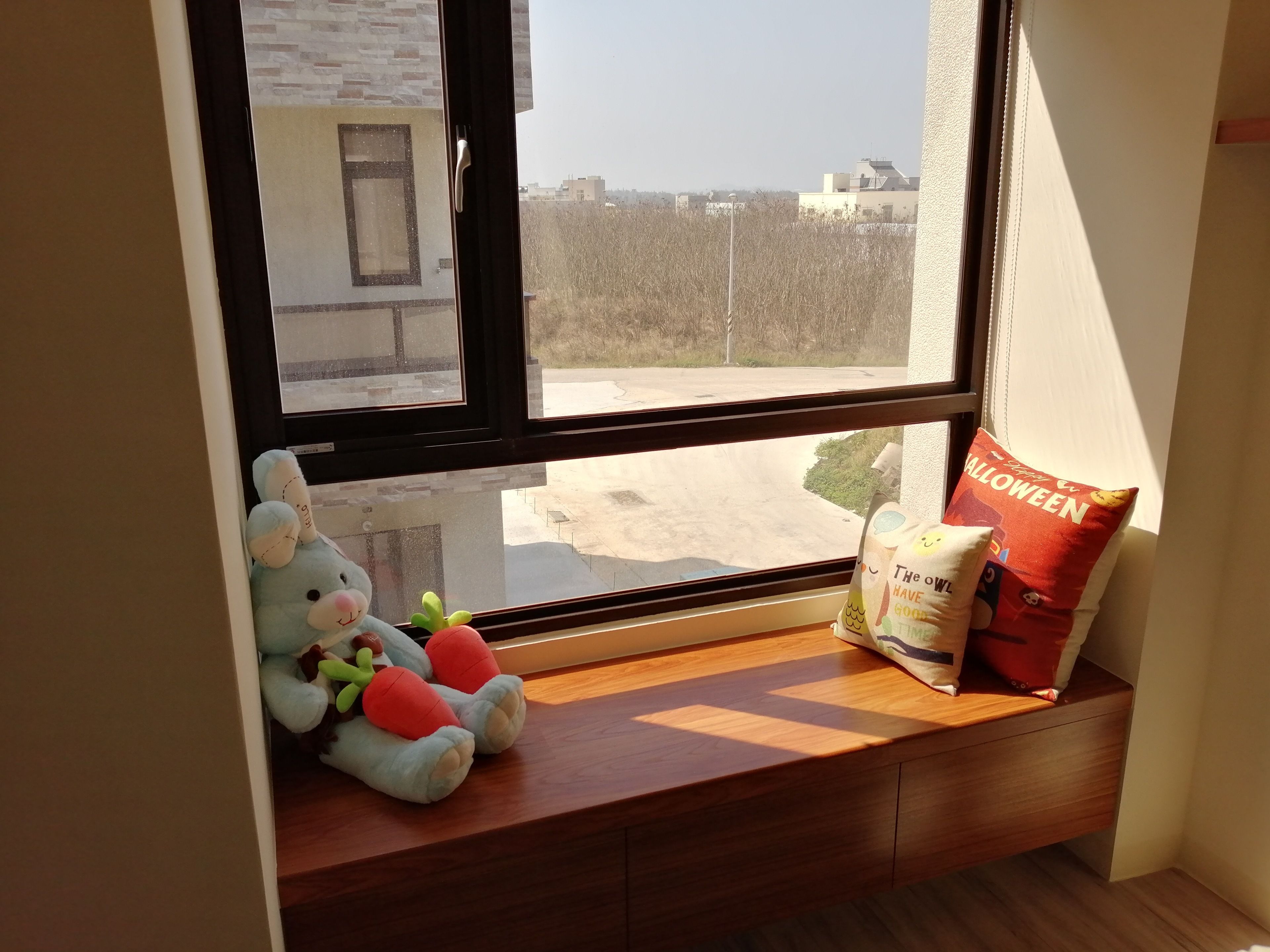 A window seat with a plush toy, a pillow, and a bag.