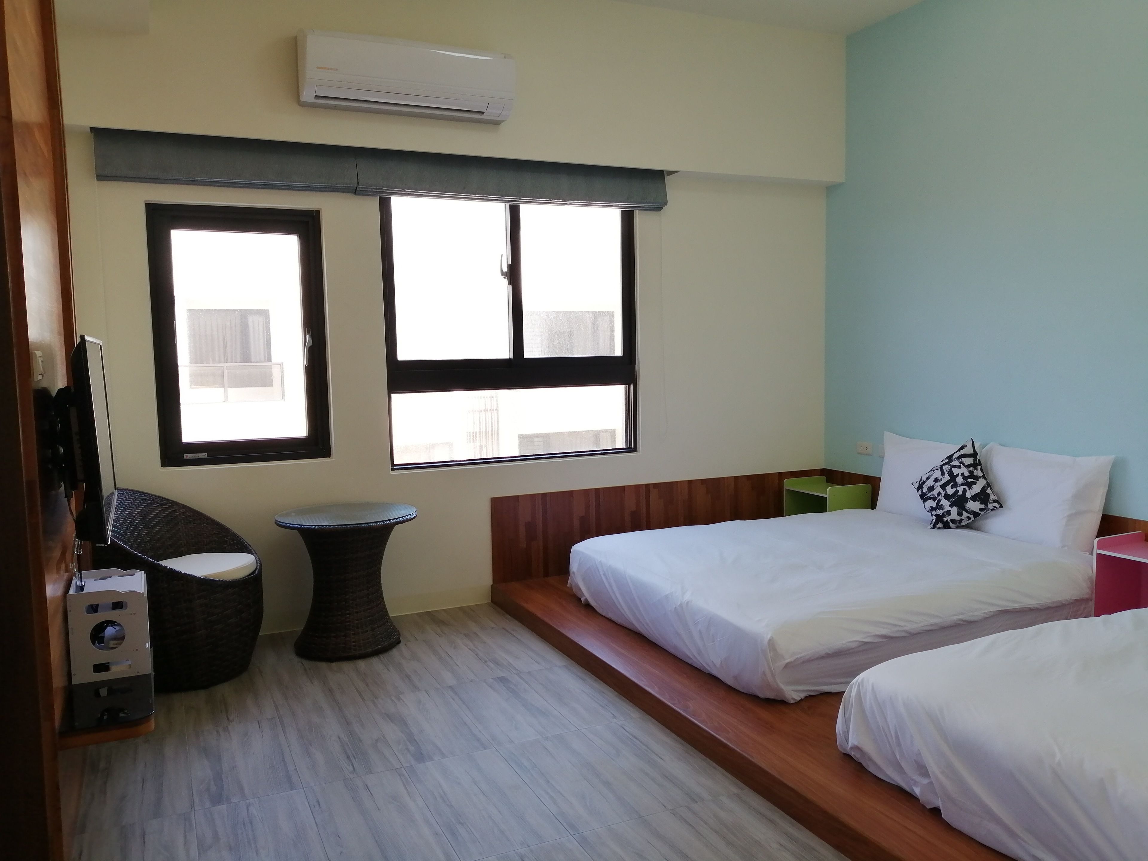 A hotel room with two beds, a small round table, a large window, and an air conditioning unit.