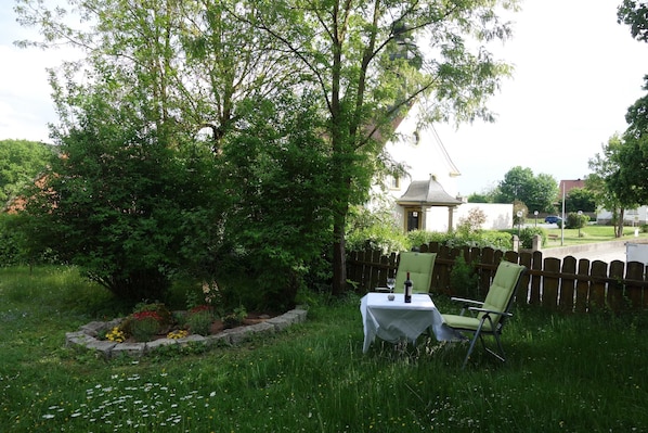 A garden with a table and chairs, surrounded by greenery and a wooden fence. - Vacation apartment Linde (2 persons) - Ferienwohnungen May (Plankenfels)
