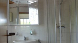 Casa de banho com lavatório branco, espelho e cabine de duche.
