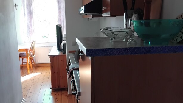 A kitchen with wooden cabinets, a countertop, and a window with curtains. - Vacation apartment Linde (2 persons) - Ferienwohnungen May (Plankenfels)