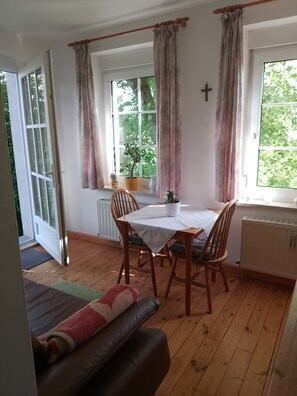 A cozy room with a dining table, chairs, a sofa, and a window with curtains. - Vacation apartment Linde (2 persons) - Ferienwohnungen May (Plankenfels)