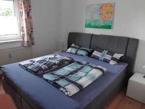 A bedroom with a bed, pillows, a bedside table, a lamp, and a window with curtains. - Vacation apartment Linde (2 persons) - Ferienwohnungen May (Plankenfels)