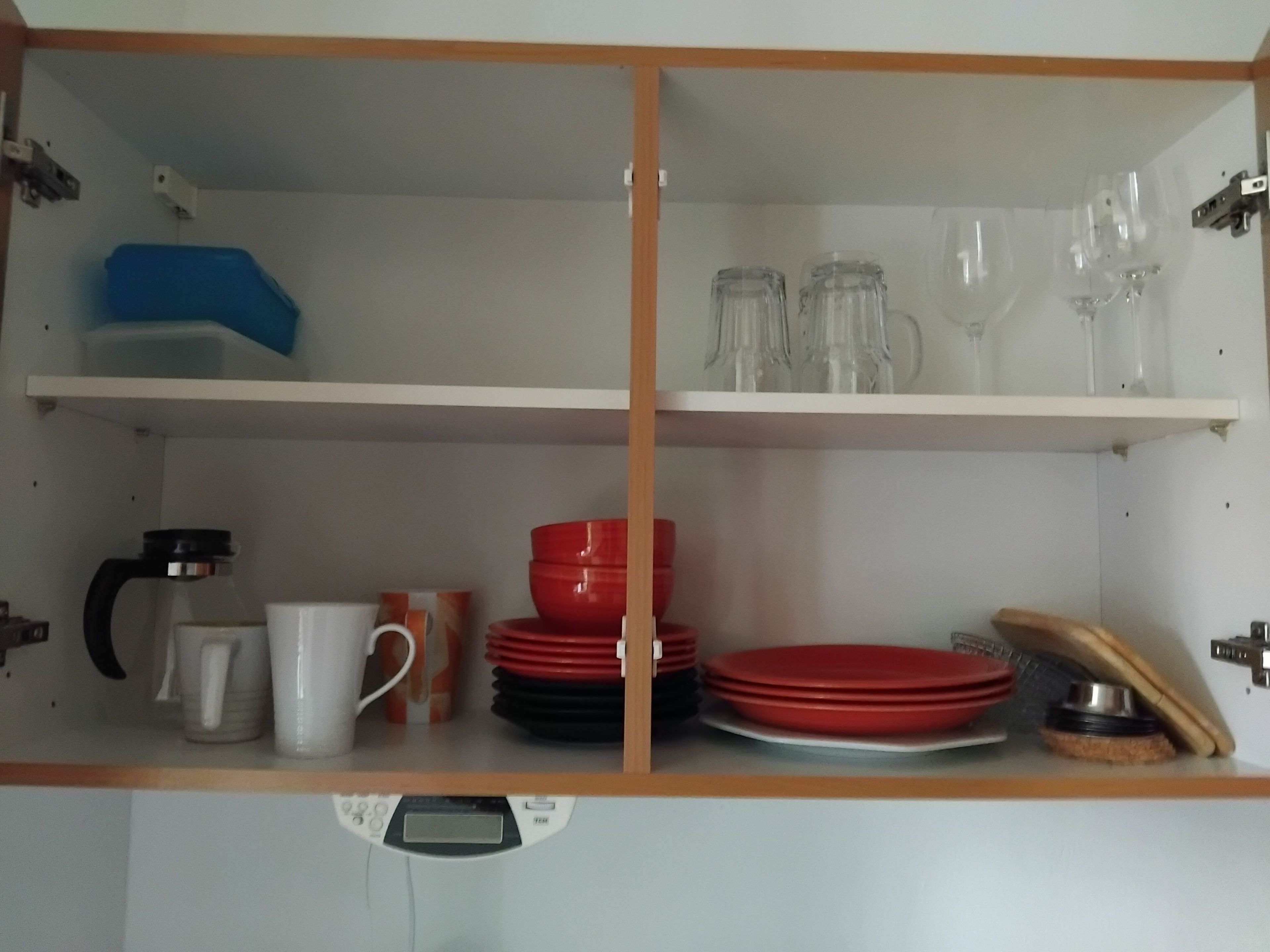 Eine Küche mit zwei Regalen, auf dem einen Tassen und eine Kaffeemaschine, auf dem anderen Teller und Gläser.