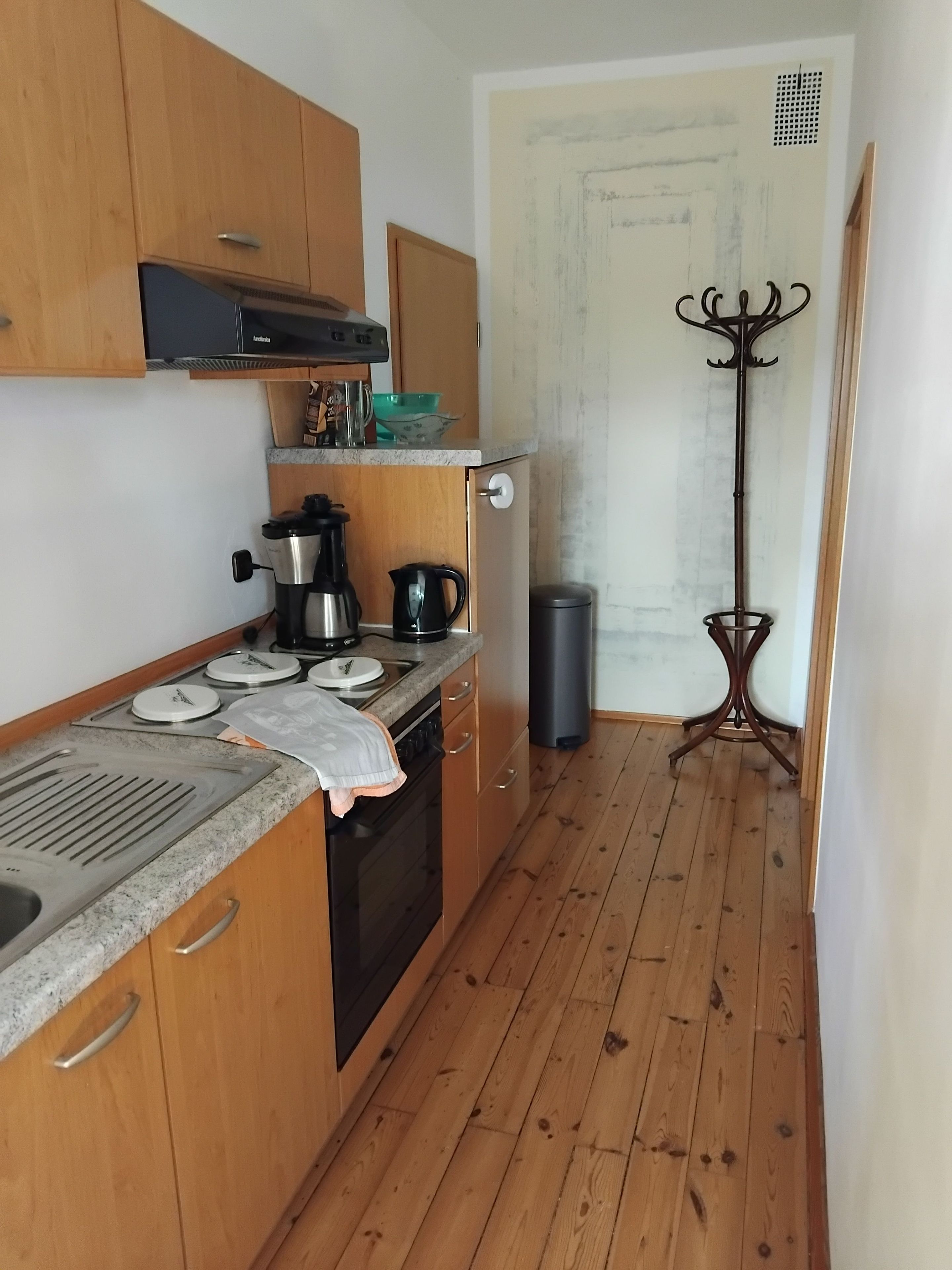 Pieni, käytännöllinen keittiö, jossa on puukehikoiset kaapit, liesi, pesuallas ja roskakori.