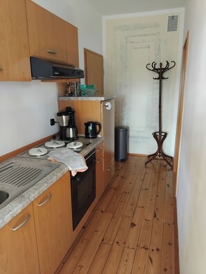 A compact kitchen with wooden cabinets, a stove, a sink, and a trash bin. - Vacation apartment Linde (2 persons) - Ferienwohnungen May (Plankenfels)